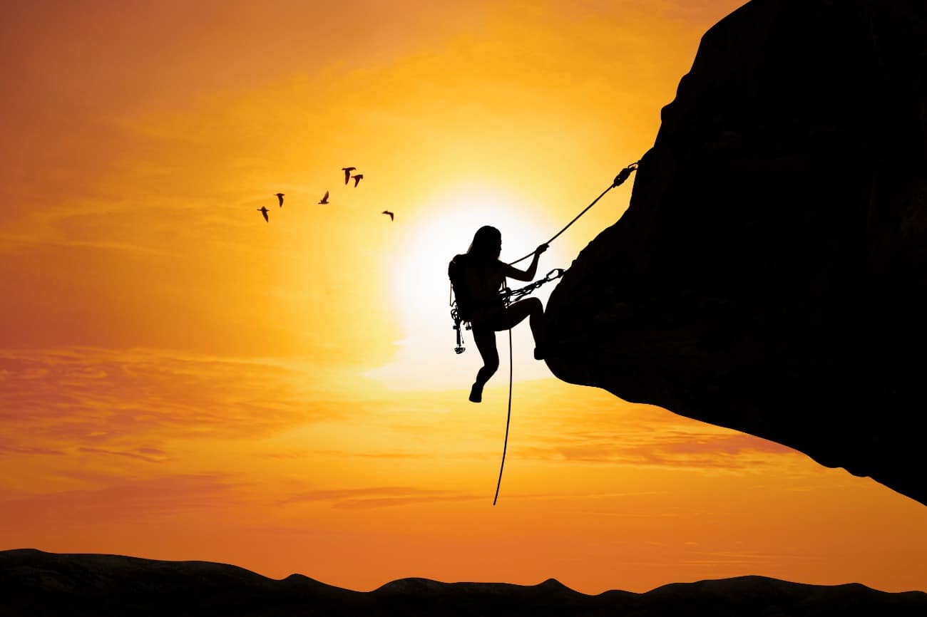 Woman silhouette rock climbing in front of sunrise