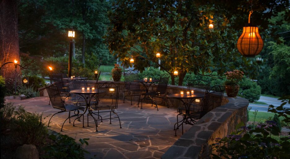 The back patio of the Chanticleer Inn shows candlelit tables in a dense garden at dusk.