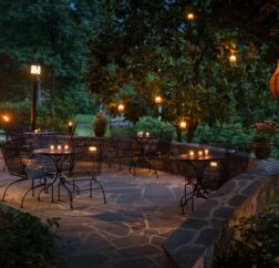 The back patio of the Chanticleer Inn shows candlelit tables in a dense garden at dusk.