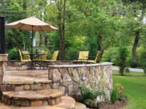 Chairs rest on the stone covered Chanticleer Inn with lush forests in the background and colorful flowers in the flower bed.