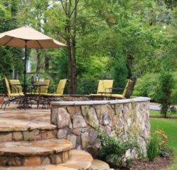 Chairs rest on the stone covered Chanticleer Inn with lush forests in the background and colorful flowers in the flower bed.