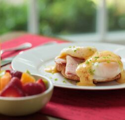 An Eggs Benedict with fresh fruit and orange juice.
