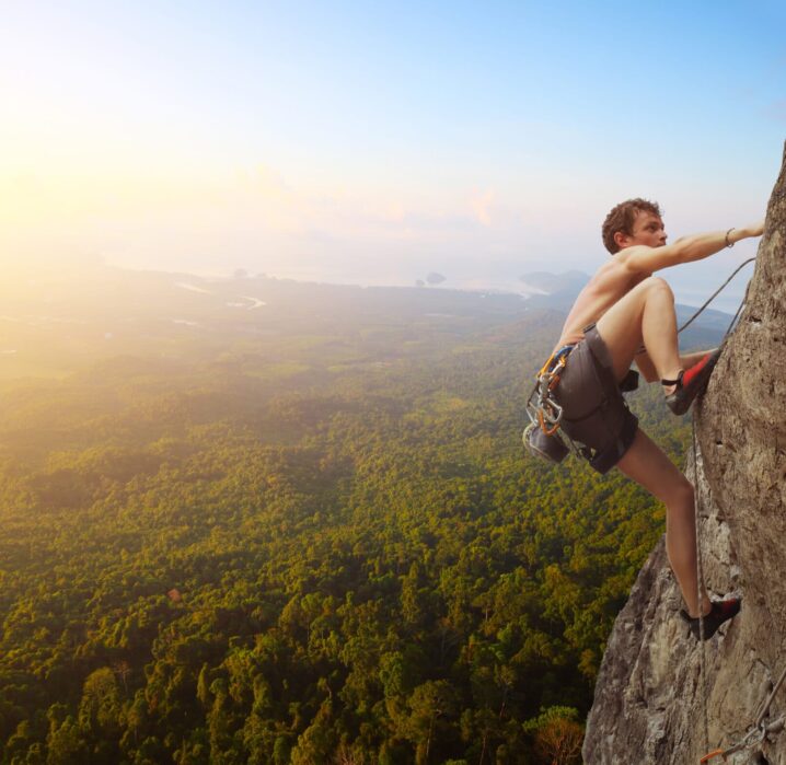 Young man climbs on a rocky wall in a valley with mountains at sunrise