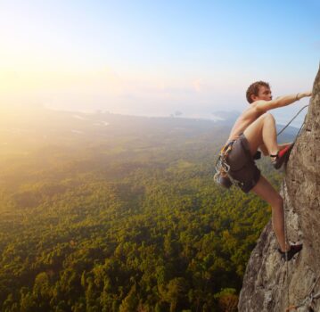 Young man climbs on a rocky wall in a valley with mountains at sunrise